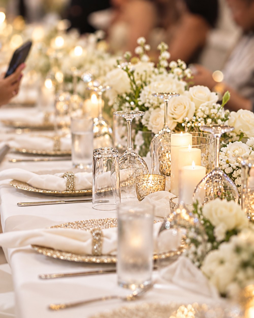 A long table set for a celebration with white roses, candles and gold chargers.
